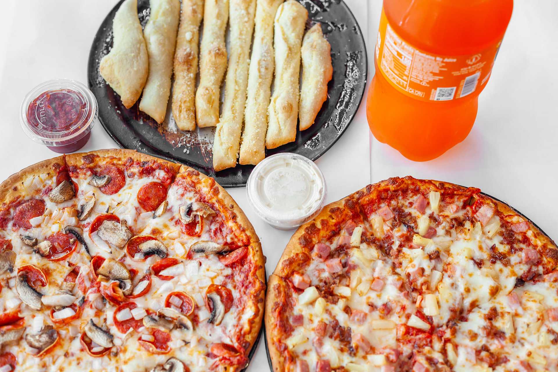 pizza, bread sticks, dips and soda on a table